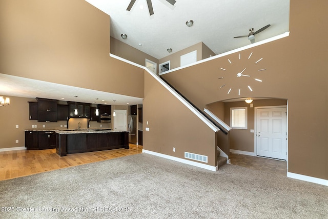 unfurnished living room featuring a towering ceiling, ceiling fan with notable chandelier, and light carpet