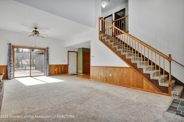 unfurnished living room featuring ceiling fan, light carpet, and wood walls