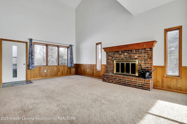 unfurnished living room with a brick fireplace, wooden walls, high vaulted ceiling, and carpet flooring