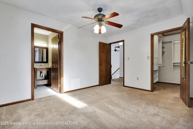 unfurnished bedroom with light colored carpet, a closet, ensuite bath, and a walk in closet