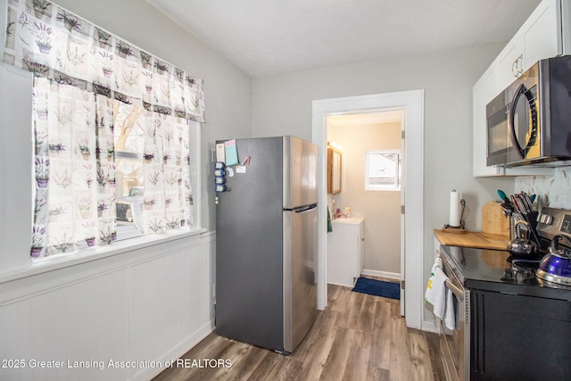 kitchen with appliances with stainless steel finishes, hardwood / wood-style floors, and white cabinets