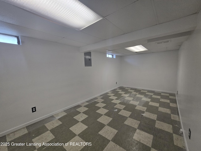 basement with a paneled ceiling and electric panel