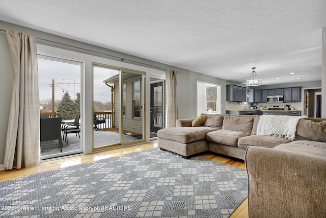 living room featuring plenty of natural light, a chandelier, a textured ceiling, and light wood-type flooring