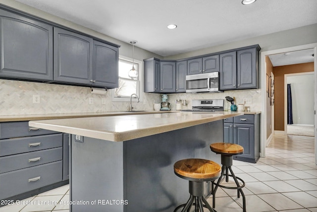 kitchen with pendant lighting, light tile patterned floors, sink, appliances with stainless steel finishes, and a center island