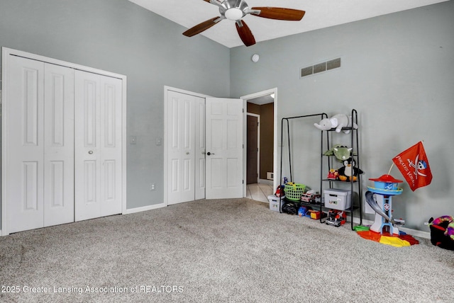 bedroom with ceiling fan, carpet flooring, two closets, and high vaulted ceiling