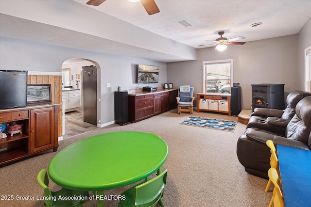 carpeted living room featuring a wood stove, a wealth of natural light, and ceiling fan