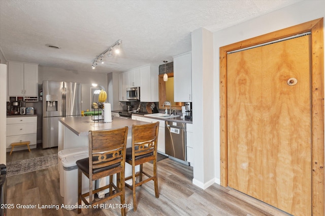 kitchen with sink, white cabinetry, hanging light fixtures, stainless steel appliances, and light hardwood / wood-style floors