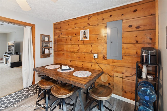 dining space featuring hardwood / wood-style flooring, electric panel, a textured ceiling, and wood walls