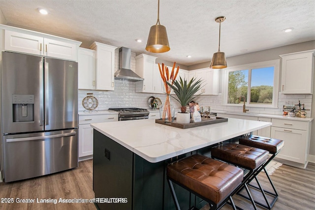 kitchen featuring appliances with stainless steel finishes, decorative light fixtures, white cabinetry, sink, and wall chimney exhaust hood