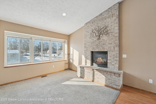 unfurnished living room with lofted ceiling, hardwood / wood-style floors, a textured ceiling, and a fireplace