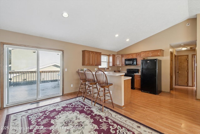 kitchen with black appliances, lofted ceiling, a breakfast bar area, light hardwood / wood-style floors, and kitchen peninsula