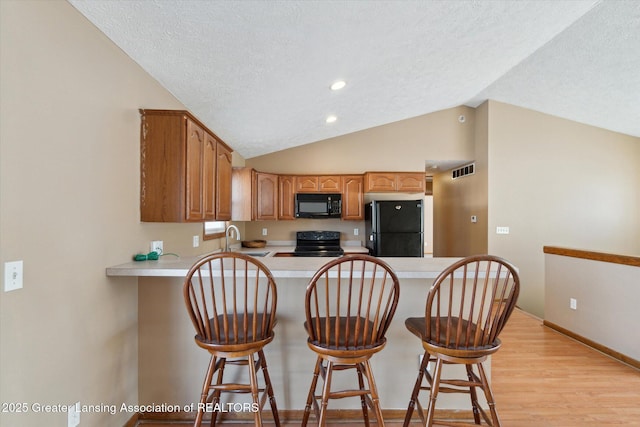 kitchen with sink, kitchen peninsula, a kitchen bar, and black appliances