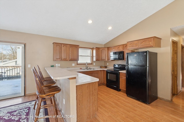 kitchen with vaulted ceiling, black appliances, sink, a kitchen bar, and kitchen peninsula