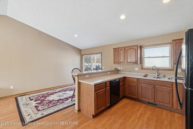 kitchen featuring lofted ceiling, sink, light wood-type flooring, kitchen peninsula, and black appliances