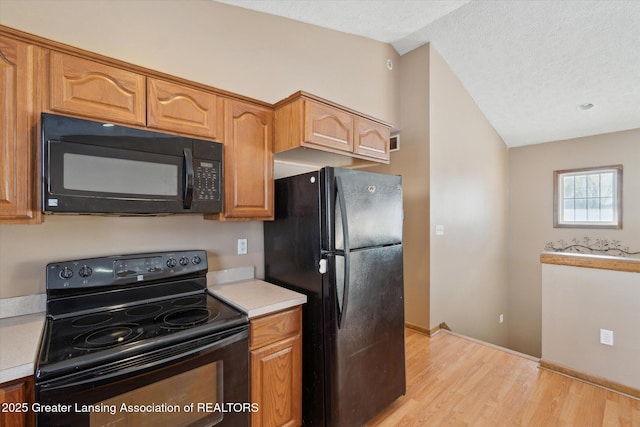 kitchen with lofted ceiling, light hardwood / wood-style flooring, black appliances, and a textured ceiling