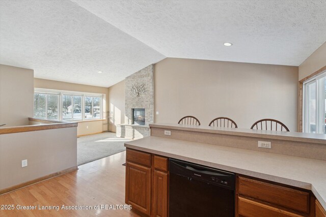 kitchen with dishwasher, lofted ceiling, light wood-type flooring, a brick fireplace, and a textured ceiling