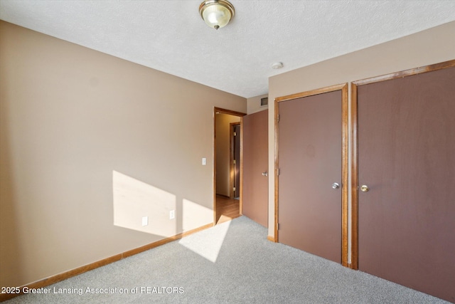 unfurnished bedroom with multiple closets, light colored carpet, and a textured ceiling