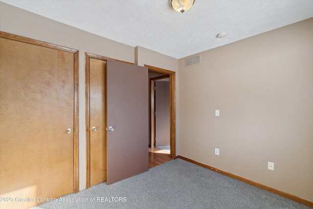 unfurnished bedroom featuring carpet floors, a textured ceiling, and two closets