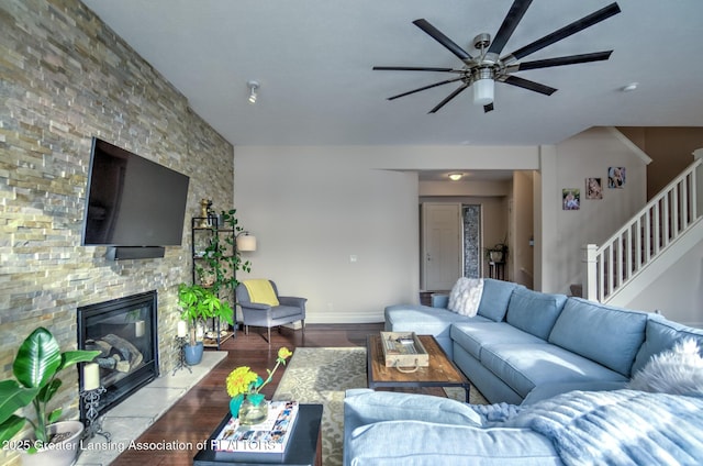 living room featuring ceiling fan, a stone fireplace, and light hardwood / wood-style floors