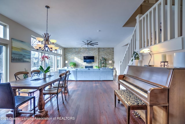 dining room with a stone fireplace, ceiling fan with notable chandelier, and dark hardwood / wood-style floors