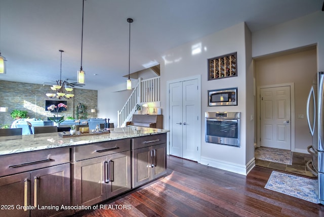 kitchen with appliances with stainless steel finishes, decorative light fixtures, dark brown cabinetry, light stone countertops, and dark wood-type flooring