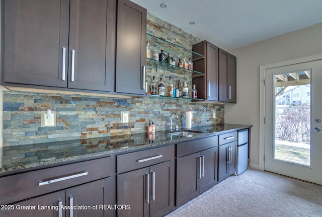 bar with sink, backsplash, dark brown cabinets, and dark stone counters