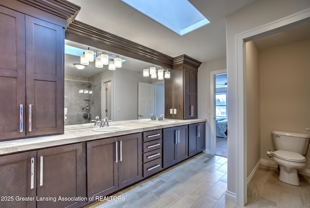 bathroom with vanity, a skylight, toilet, and tiled shower