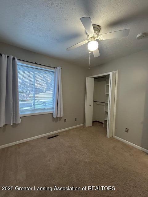 unfurnished bedroom with ceiling fan, carpet, a textured ceiling, and a closet