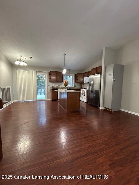 kitchen with white appliances, dark wood-type flooring, a kitchen island, decorative light fixtures, and vaulted ceiling