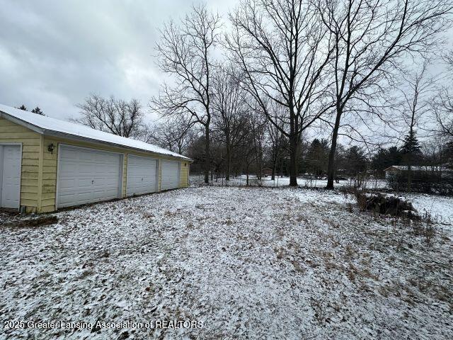 yard covered in snow featuring a garage and an outdoor structure