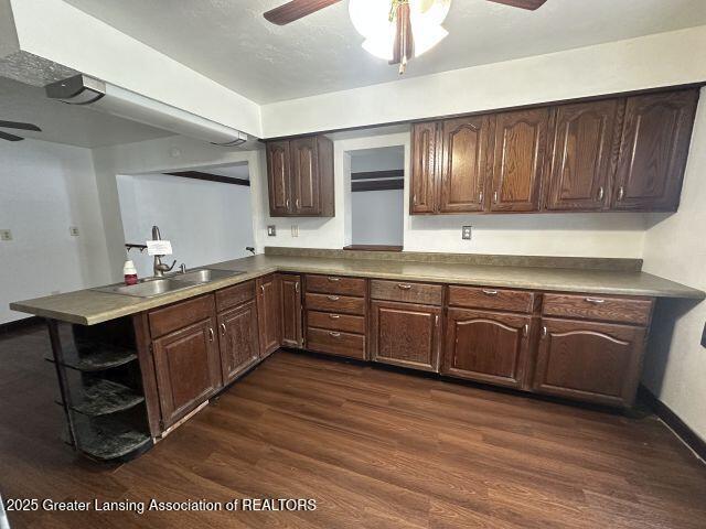 kitchen featuring kitchen peninsula, sink, dark brown cabinetry, ceiling fan, and dark wood-type flooring