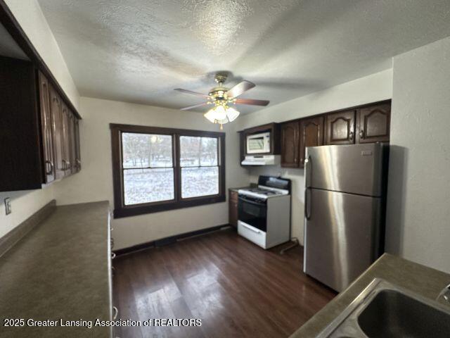 kitchen with stainless steel fridge, dark brown cabinetry, white stove, dark wood-type flooring, and a textured ceiling