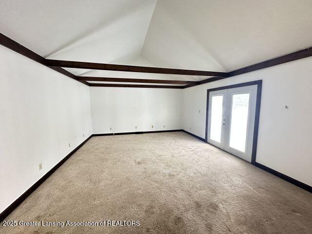 carpeted empty room featuring vaulted ceiling with beams and french doors