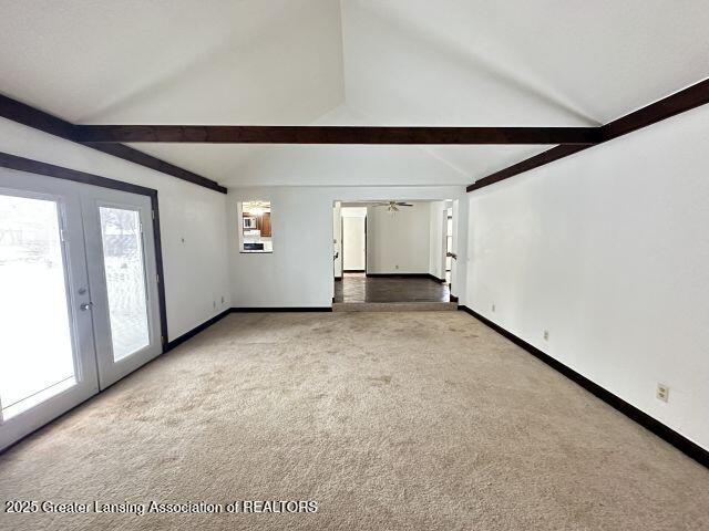 unfurnished living room featuring beamed ceiling, carpet floors, high vaulted ceiling, and french doors