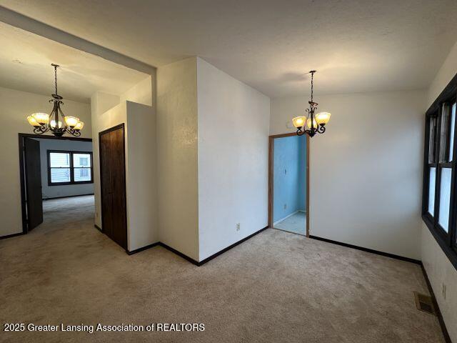 carpeted spare room featuring a chandelier