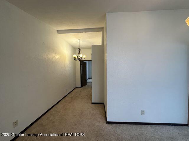 corridor with light carpet and a notable chandelier