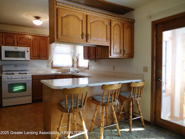 kitchen featuring a kitchen breakfast bar, sink, white appliances, and kitchen peninsula