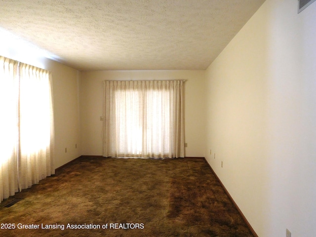 spare room with dark colored carpet, a healthy amount of sunlight, and a textured ceiling