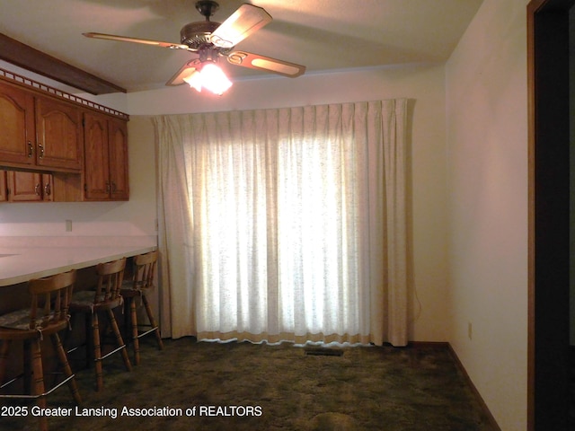 unfurnished dining area featuring dark carpet and ceiling fan