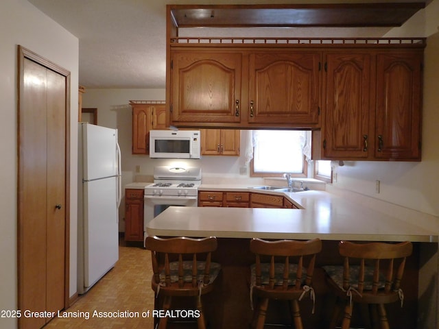 kitchen featuring a kitchen breakfast bar, sink, white appliances, and kitchen peninsula