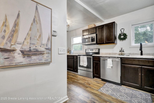 kitchen featuring appliances with stainless steel finishes, sink, dark brown cabinetry, beam ceiling, and light hardwood / wood-style flooring