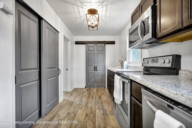 kitchen featuring dark brown cabinets, pendant lighting, stainless steel appliances, a barn door, and light hardwood / wood-style floors