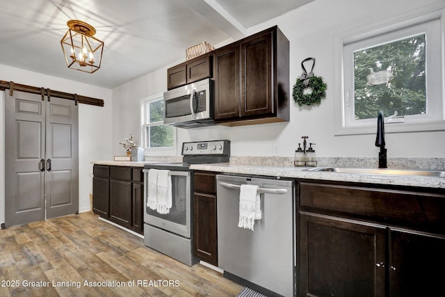 kitchen featuring sink, appliances with stainless steel finishes, hanging light fixtures, a barn door, and light wood-type flooring