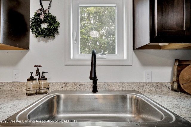 interior details featuring sink, dark brown cabinets, and light stone countertops