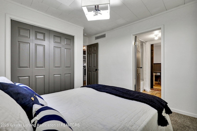 carpeted bedroom featuring ornamental molding, ensuite bathroom, and a closet