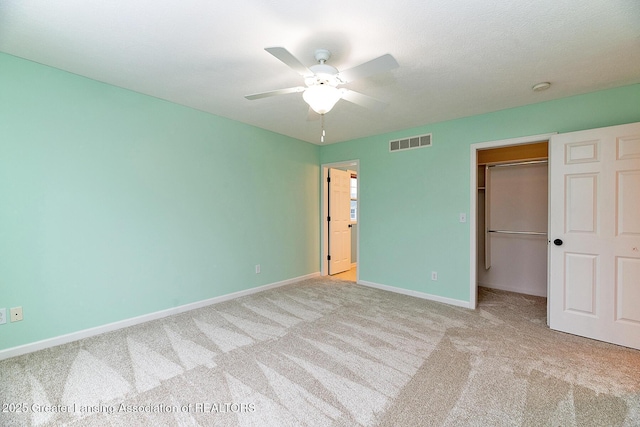 unfurnished bedroom featuring light carpet, a walk in closet, a closet, and ceiling fan