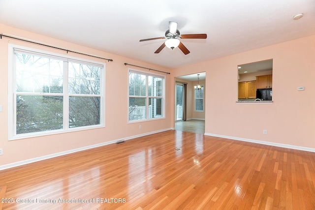 unfurnished living room featuring ceiling fan with notable chandelier and light wood-type flooring