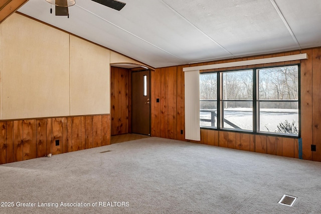 carpeted empty room featuring vaulted ceiling and wood walls