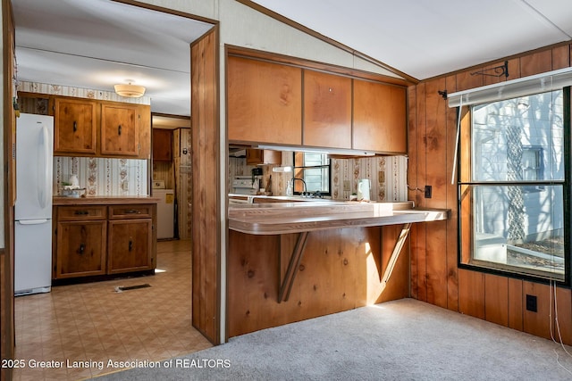 kitchen with wooden walls, lofted ceiling, washer / dryer, white refrigerator, and kitchen peninsula