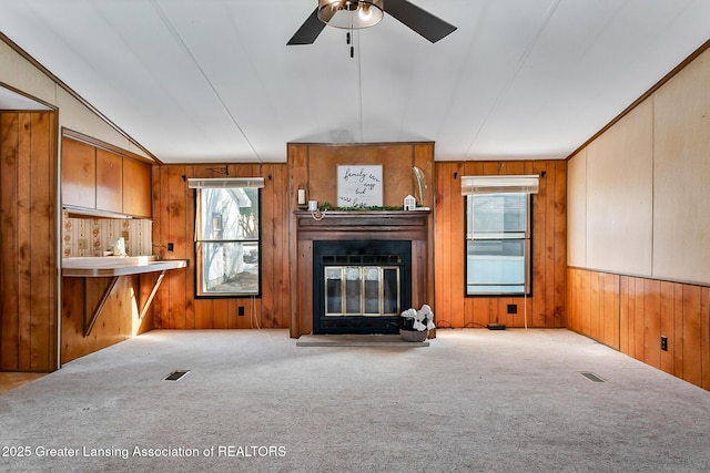 unfurnished living room featuring vaulted ceiling, light colored carpet, ceiling fan, and wood walls